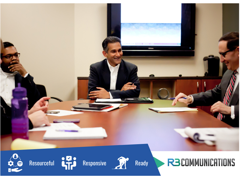 Image for R3 Communications, team members sitting around an office desk.